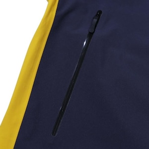 May include: Close-up of a navy blue jacket with a yellow side panel. The jacket has a black zipper and a black zippered pocket. The jacket is made of a smooth, possibly waterproof material.