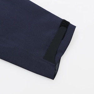 May include: Close-up of a navy blue garment sleeve with a yellow accent and a black Velcro closure. The fabric appears to be a smooth, possibly water-resistant material.