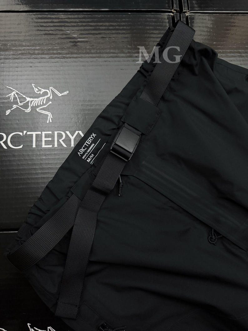 Puede incluir: Pantalones deportivos negros con cintur&oacute;n negro ajustable y hebilla. Los pantalones tienen un peque&ntilde;o bolsillo con cremallera y la marca "Arc'teryx" es visible. Los pantalones est&aacute;n hechos de un material ligero.