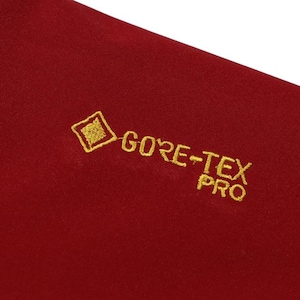 May include: Close-up of a section of red fabric with the embroidered text "GORE-TEX PRO" in gold. The fabric has a slightly textured appearance.