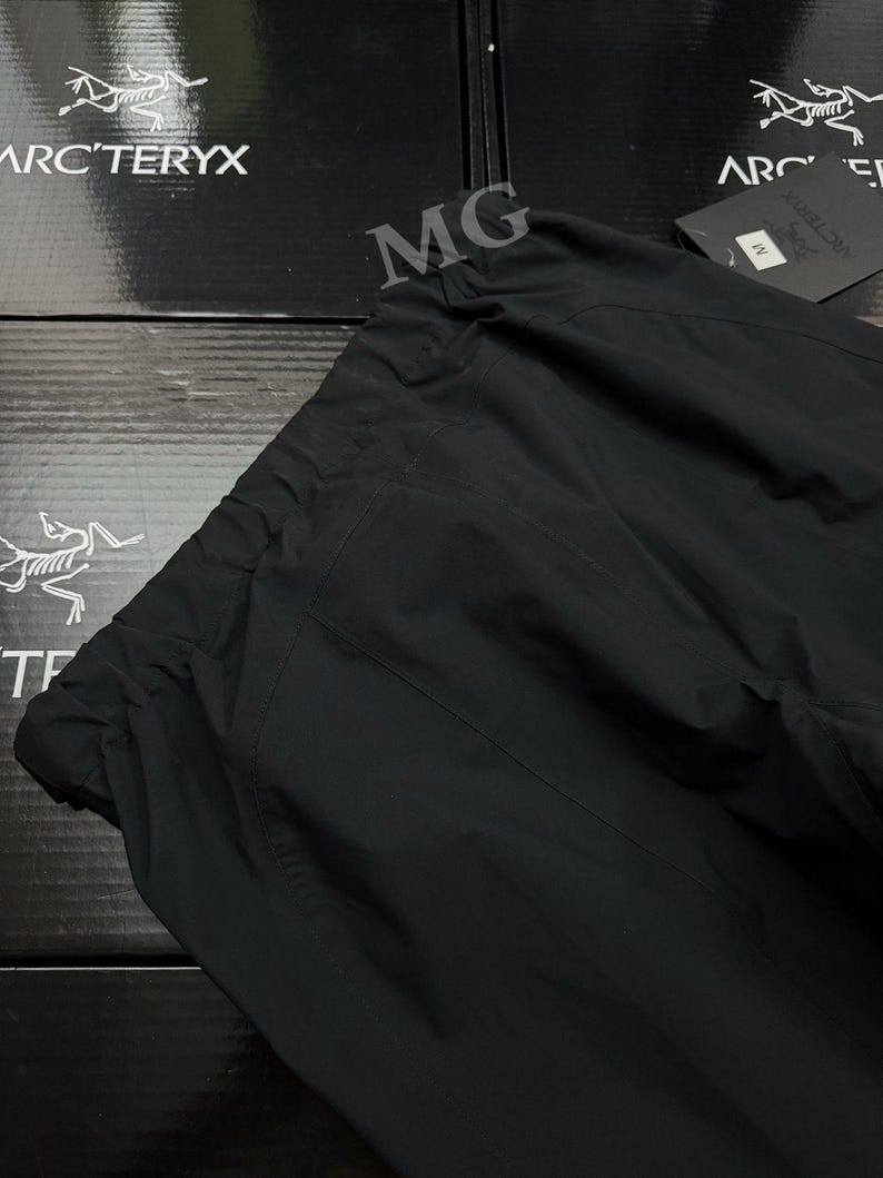 Puede incluir: Pantalones negros para exteriores con cintura con cord&oacute;n. Los pantalones est&aacute;n hechos de una tela lisa y mate. El logotipo de Arc'teryx es visible en la caja en el fondo.