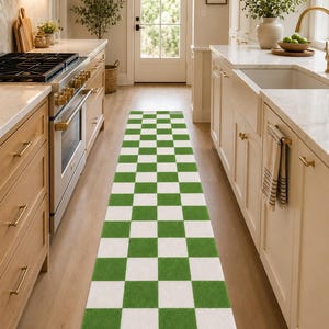 May include: A long, rectangular runner rug featuring a repeating checkered pattern of alternating grass green and white squares. The rug is positioned centrally on a wooden floor, extending lengthwise through the middle of a kitchen space.