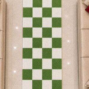 May include: A rectangular runner rug featuring a repeating checkerboard pattern of alternating grass green and white squares. The rug has a textured, pile-like surface and is oriented vertically, displaying a grid of three columns and nine rows.