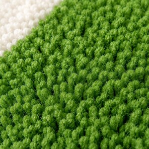 May include: A high-pile rug featuring a diagonal color block design with a vibrant green section and a contrasting off-white section. The surface is composed of dense, upright tufted loops that create a textured, soft, and plush appearance.