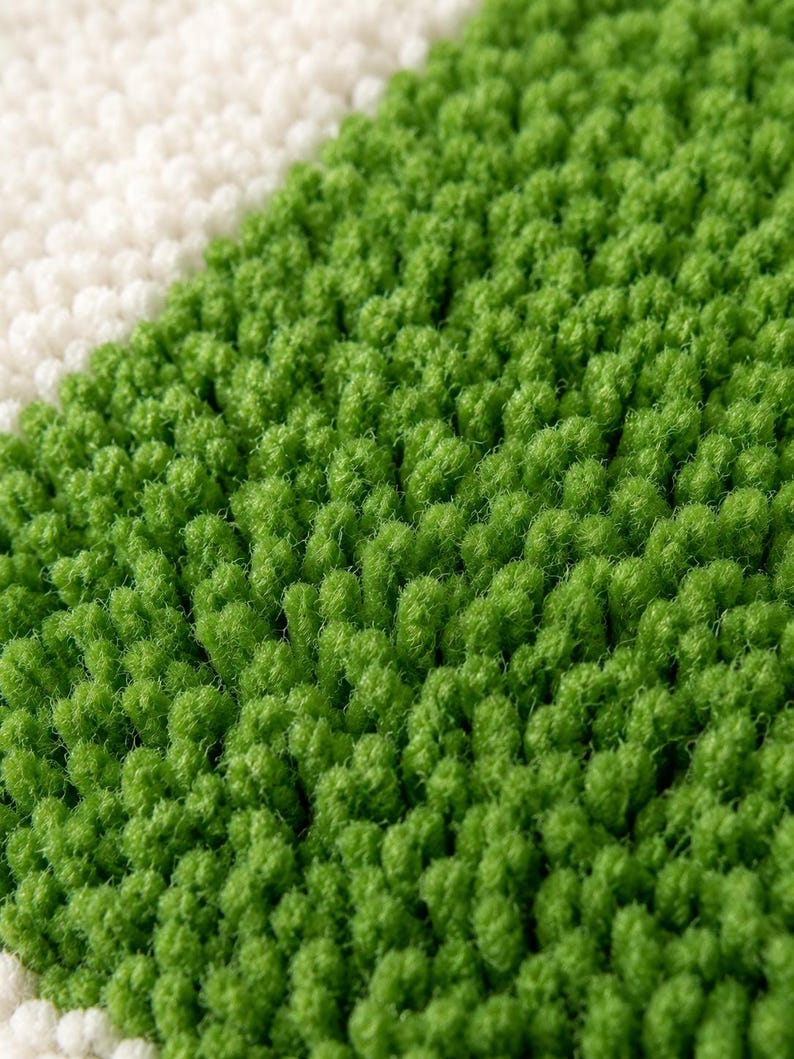 May include: A high-pile rug featuring a diagonal color block design with a vibrant green section and a contrasting off-white section. The surface is composed of dense, upright tufted loops that create a textured, soft, and plush appearance.