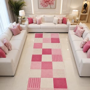 Könnte beinhalten: Ein rechteckiger Teppich mit einem geometrischen Schachbrettmuster in den Farben Hellrosa, Dunkelrosa und Creme. Das Design wechselt zwischen einfarbigen Quadraten und Quadraten mit einem strukturierten, horizontalen Streifenmuster.