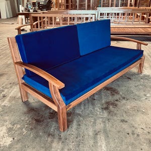 May include: A wooden two-seater sofa with a deep blue velvet cushion and backrest. The sofa has a natural wood finish and curved armrests. The design is modern and suitable for a patio or garden.