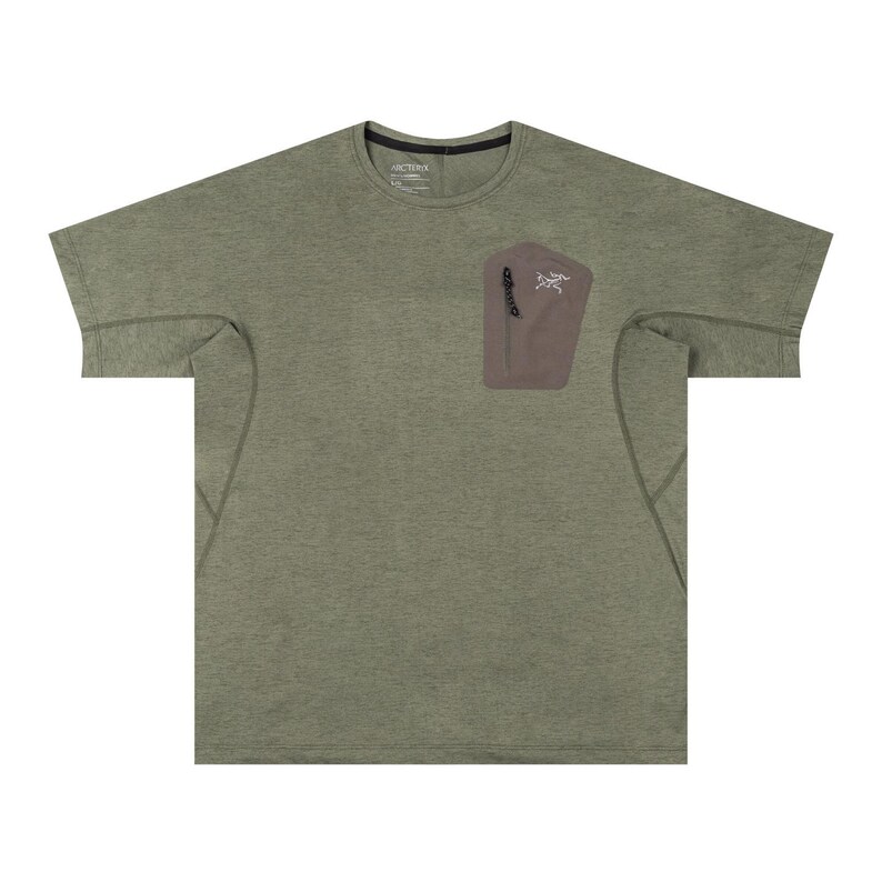 May include: Olive green short-sleeve t-shirt with a small, brown pocket on the chest. The pocket has a zipper and a white logo. The shirt has a crew neck and a relaxed fit.