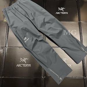 May include: Gray Arc'teryx rain pants with a drawstring waist and zippered pockets. The pants have the Arc'teryx logo on the left leg and zippers at the ankles. The pants are made of a lightweight, waterproof material.