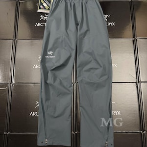 May include: Gray waterproof pants with the Arc'teryx logo on the leg. The pants have a drawstring waist and zippers along the sides of the legs. The pants are made of a durable, waterproof material.