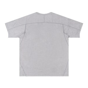 May include: A light gray short-sleeve t-shirt with a crew neck. The shirt has a relaxed fit with seams visible across the shoulders and down the back. The fabric appears to be a soft, textured material.