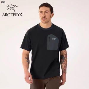 May include: Black short-sleeve t-shirt with a dark gray pocket on the chest. The pocket has a zipper and a small logo. The shirt has a crew neck with a dark blue trim. The brand name "ARC'TERYX" is printed on the shirt.
