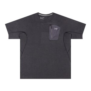 May include: Dark gray short-sleeve shirt with a small zippered pocket on the chest. The pocket is a lighter shade of gray and features a white logo. The shirt has a crew neck and a subtle texture.