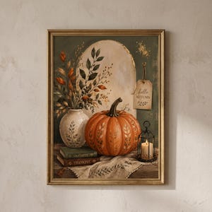 Op de afbeelding: Een ingelijste wandkunstprint met een grote oranje pompoen met geschilderde bladmotieven, een witte vaas met herfstbladeren, twee gestapelde boeken met de tekst Grateful en Thankful, een brandende kaars in een zwarte kooi en een label met hello AUTUMN.