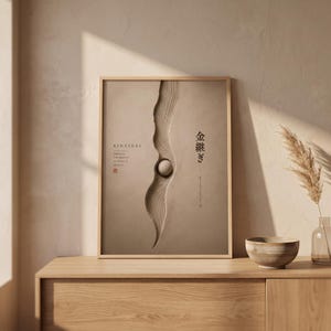 Può includere: Una stampa murale rettangolare incorniciata in tonalità beige con una scanalatura verticale centrale testurizzata e una piccola sfera. Il testo recita KINTSUGI, EMBRACE THE BEAUTY OF WHAT IS BROKEN, e caratteri giapponesi.