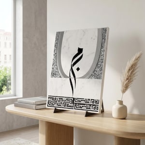 May include: A rectangular wall art piece featuring a white marble background with a central black Arabic calligraphy character. The design includes a grey arched border, a textured silver section, and a black geometric Kufic script at the bottom.