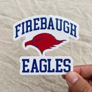 May include: A white sticker with the words "FIREBAUGH" in blue block letters arched across the top and "EAGLES" at the bottom. A red eagle head is centered between the words. The sticker is held by a hand.