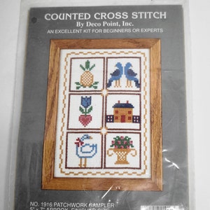 May include: A counted cross stitch kit featuring a patchwork sampler with a pineapple, birds, a tulip, a house, a duck, and a basket of flowers. The kit includes 14 count 100% cotton Aida cloth, embroidery floss, a needle, a graph, and instructions. The finished size is 5 inches by 7 inches. The frame is not included. The kit is by Deco Point, Inc. and is from 1989.