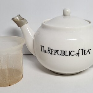 May include: White ceramic teapot with a silver lid and spout. The teapot has a mesh strainer and the words "The Republic of Tea" printed on the side.
