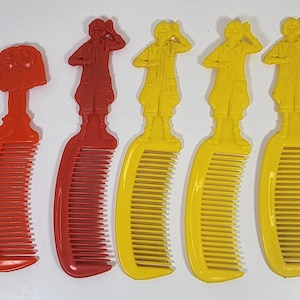 May include: Five plastic combs with cartoon figures on the handles. Two combs are red with a cartoon figure of a girl with red hair. Three combs are yellow with a cartoon figure of a boy with yellow hair.