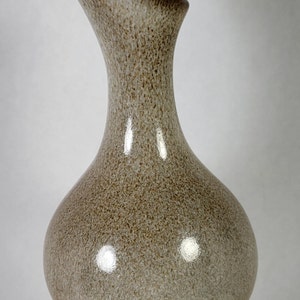 May include: A brown and white ceramic vase with a speckled glaze. The vase has a wide, round base and a narrow neck that curves upwards.