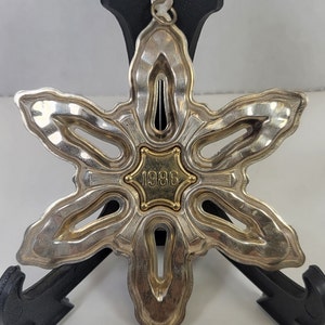May include: Silver snowflake Christmas ornament with a gold center featuring the year 1986.