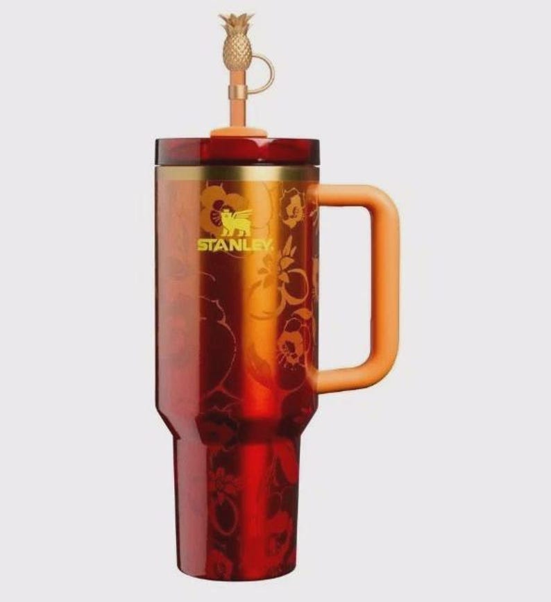 May include: A red and orange Stanley tumbler with a handle and a pineapple-shaped topper. The tumbler features a floral design and the Stanley logo in gold. The handle and topper are orange.