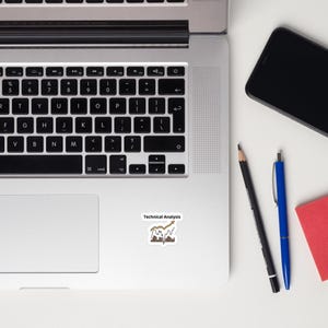May include: A sticker with the text "Technical Analysis" and a graphic of a rising stock chart is placed on a laptop. A black pencil, a blue pen, and a smartphone are also visible.