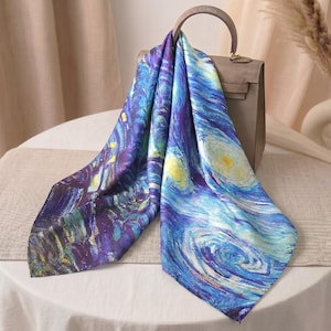 May include: A silk scarf featuring a vibrant print inspired by Van Gogh's "Starry Night." The scarf displays swirling blues, yellows, and purples, draped over a taupe handbag. The artwork is a beautiful accessory.
