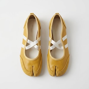 May include: A pair of mustard yellow split-toe shoes with white crisscross straps. The shoes have a suede toe cap and a leather upper. The design is a modern take on a traditional style, suitable for casual wear.