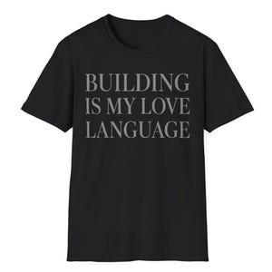 May include: A black short-sleeved t-shirt featuring the text "BUILDING IS MY LOVE LANGUAGE" printed in a grey, serif font across the center of the chest. The garment has a crew neckline and a standard fit with straight hemline and sleeves.