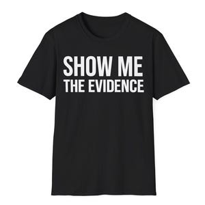 May include: A black short-sleeved t-shirt featuring the white text SHOW ME THE EVIDENCE printed in a bold, sans-serif font across the chest. The garment has a classic crew neckline and a straight hemline, presenting a simple and clean design.