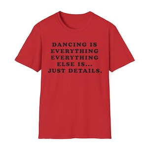 May include: A bright red short-sleeved t-shirt featuring black text centered on the chest that reads: DANCING IS EVERYTHING EVERYTHING EVERYTHING ELSE IS... JUST DETAILS. The garment has a classic crew neckline and a standard fit.