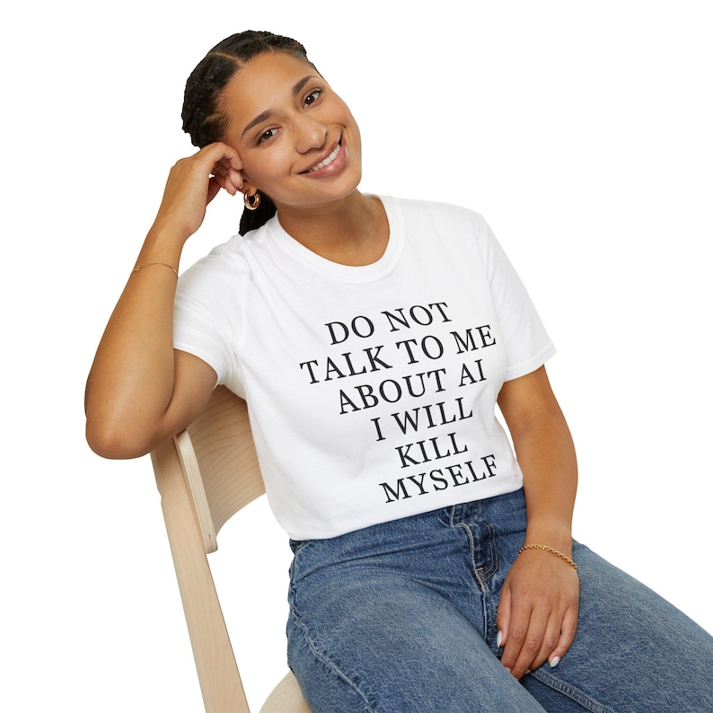May include: A white short-sleeved t-shirt featuring black text printed on the front that reads: DO NOT TALK TO ME ABOUT AI I WILL KILL MYSELF. The shirt is paired with blue denim jeans.