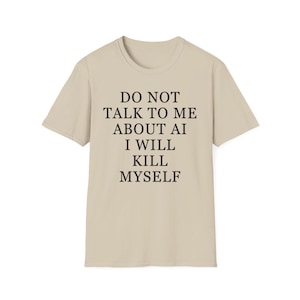May include: A beige short-sleeved t-shirt featuring black text printed on the front that reads: DO NOT TALK TO ME ABOUT AI I WILL KILL MYSELF. The garment has a crew neckline and a standard fit, presented against a plain, neutral background.