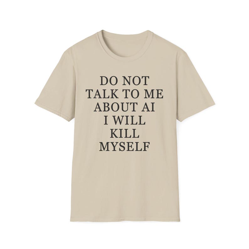 May include: A beige short-sleeved t-shirt featuring black text printed on the front that reads: DO NOT TALK TO ME ABOUT AI I WILL KILL MYSELF. The garment has a crew neckline and a standard fit, presented against a plain, neutral background.