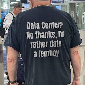 Pode incluir: Uma t-shirt preta de manga curta com texto branco de estilo desgastado impresso nas costas que diz: Data Center? No thanks, I'd rather date a femboy. A t-shirt apresenta um decote redondo e um corte padrão, exibindo o texto claramente.