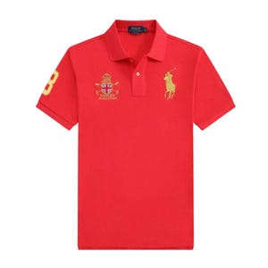 May include: A red polo shirt with short sleeves. The shirt features a gold number 3 on the left sleeve, a gold logo of a person on a horse, and a crest with text on the chest. The shirt has a button-down collar.