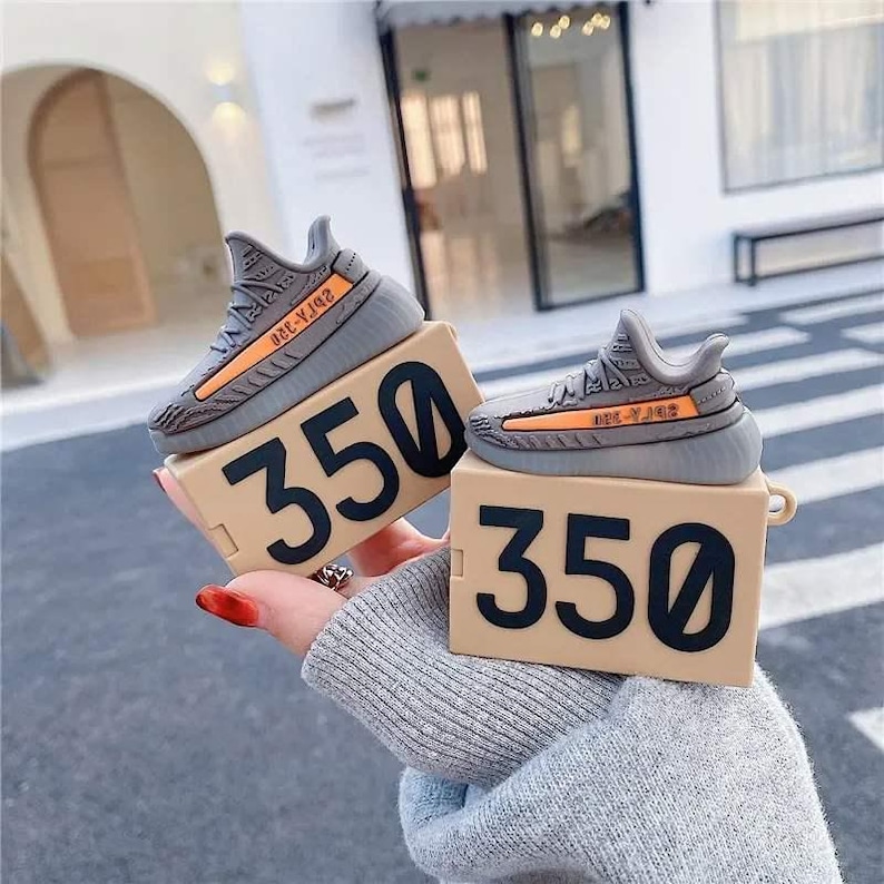 May include: Gray and orange sneaker-shaped case for wireless earbuds, resting on a tan box with the number 350 in black. The case mimics the design of a popular sneaker.