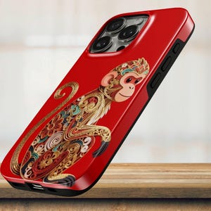 May include: A red smartphone case featuring a detailed, multi-colored monkey illustration composed of intricate, swirling patterns in gold, teal, and orange. The case has a black border, visible camera lens cutouts, and side button access points.