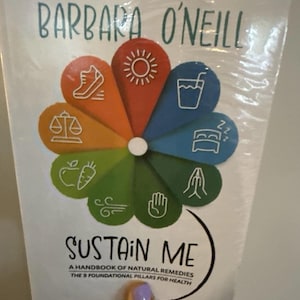Könnte beinhalten: Ein Buch mit dem Titel Sustain Me von Barbara O'Neill, A Handbook of Natural Remedies, The 9 Foundational Pillars for Health. Das Cover zeigt ein buntes, blumenförmiges Diagramm mit weißen Symbolen, die verschiedene Gesundheitssäulen darstellen.