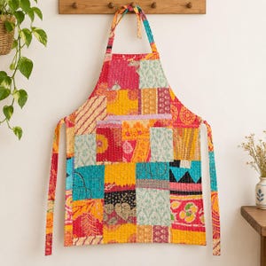 Può includere: Un grembiule trapuntato caratterizzato da un vivace design patchwork con vari quadrati di tessuto colorati nelle tonalità del rosa, giallo, turchese e nero. Il grembiule include una tasca centrale, un laccio al collo e due lacci laterali cuciti.