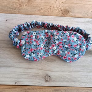 Può includere: Una mascherina per dormire floreale con sfondo azzurro e un motivo di piccoli fiori rosa e bianchi. L'elastico è azzurro abbinato con un design a balze. La mascherina è progettata per bloccare la luce per un sonno migliore.