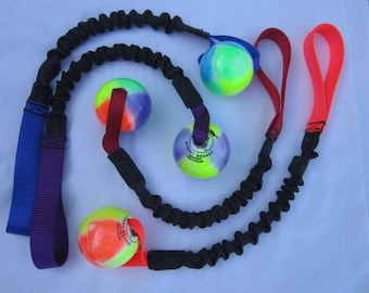 Puede incluir: Un conjunto de tres bolas coloridas, multicolores, con cordones elásticos y correas negras. Las bolas están hechas de un material suave y gomoso y tienen una superficie texturizada. Las correas están hechas de un material de nylon duradero y tienen un lazo en el extremo. Los cordones elásticos están hechos de un material elástico y extensible y tienen un color negro.