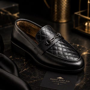 May include: A black loafer featuring a quilted vamp, a smooth leather heel and side panel, and a metallic bit ornament across the top. A small black card nearby displays the text Daily Step Co and the tagline Step Into Comfort in gold lettering.