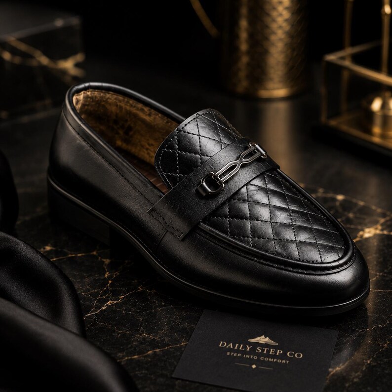 May include: A black loafer featuring a quilted vamp, a smooth leather heel and side panel, and a metallic bit ornament across the top. A small black card nearby displays the text Daily Step Co and the tagline Step Into Comfort in gold lettering.
