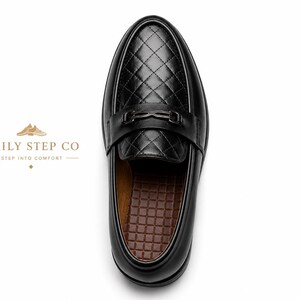 May include: A black loafer with a quilted diamond pattern on the vamp and a metallic bit across the bridge. The interior features a brown grid-textured insole. The text DAILY STEP CO STEP INTO COMFORT is visible to the left of the shoe.
