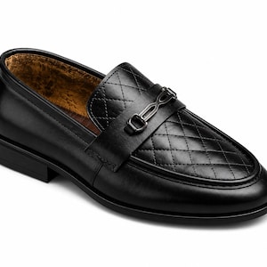 May include: A black loafer shoe featuring a quilted diamond pattern on the vamp, a smooth leather finish on the sides, and a dark metallic horsebit hardware detail across the top. The interior lining is a textured, mottled brown material.
