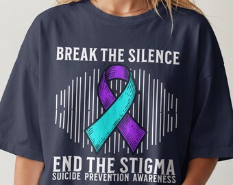 May include: A dark navy blue t-shirt featuring a teal and purple awareness ribbon graphic in the center. The text reads BREAK THE SILENCE, END THE STIGMA, and SUICIDE PREVENTION AWARENESS, surrounded by a vertical line pattern background design.