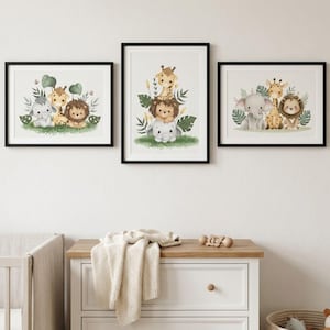 Peut inclure: Trois impressions d'art encadrées présentant des illustrations à l'aquarelle d'adorables animaux de safari. Chaque impression présente un arrangement différent d'une girafe, d'un lion et d'un éléphant, entourés de verdure. Les impressions sont affichées au-dessus d'une commode blanche.